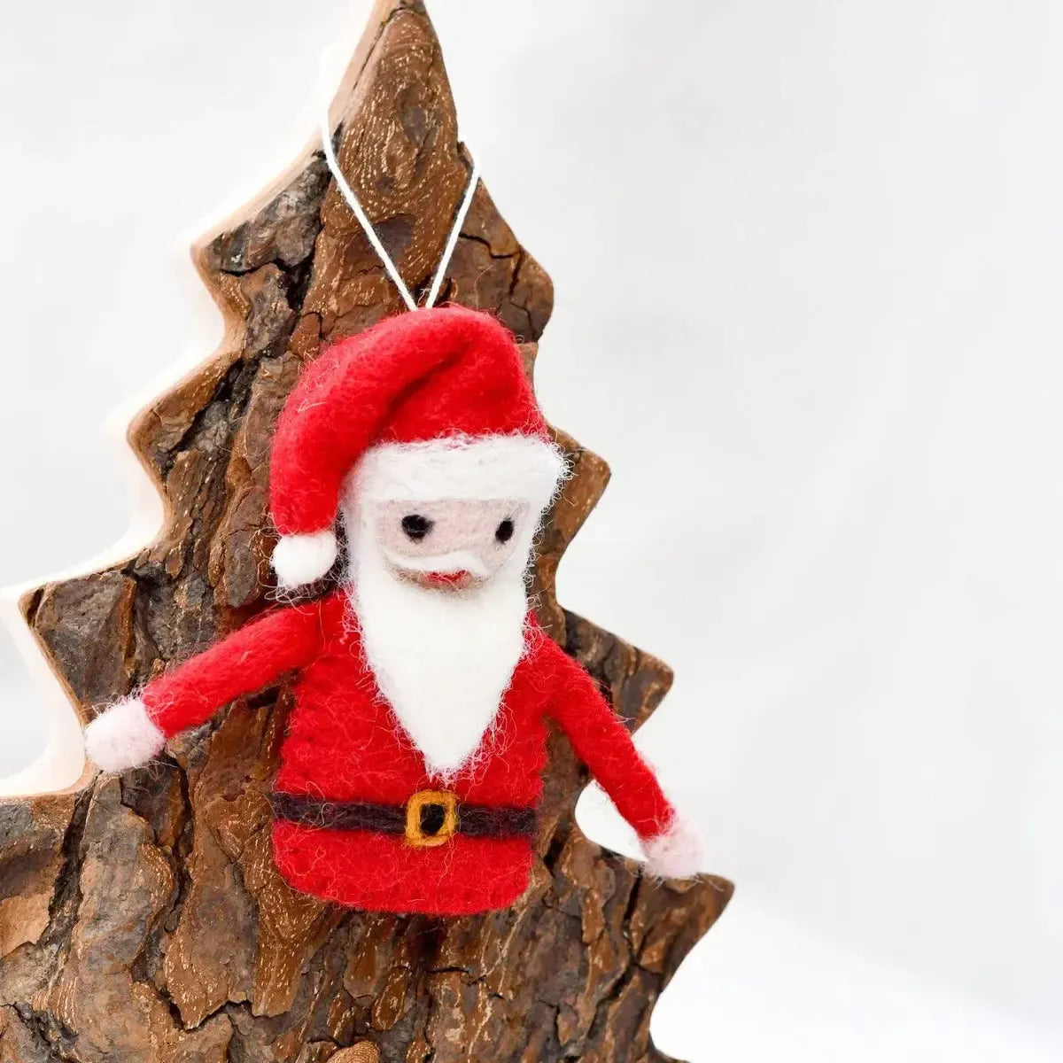 Felt Santa Claus ornament hanging on a wooden tree branch against a white background
